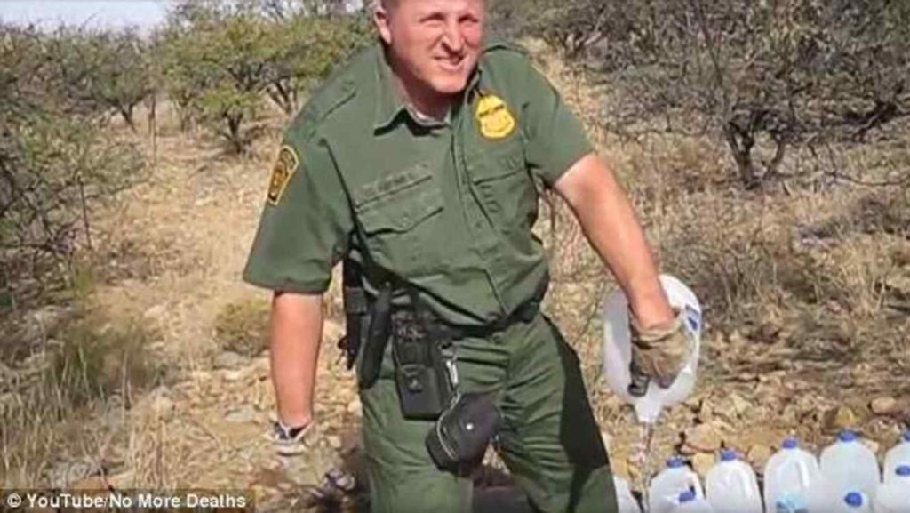 Agente fronterizo de Estados Unidos, tirando agua dejada en el decierto para migrantes.