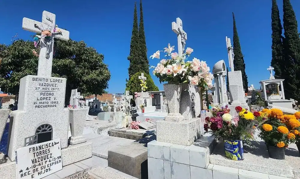 F ó tam graves y monumentos en cementerio con flores y símbolos religiosos en un día soleado.