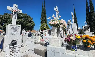 F ó tam graves y monumentos en cementerio con flores y símbolos religiosos en un día soleado.