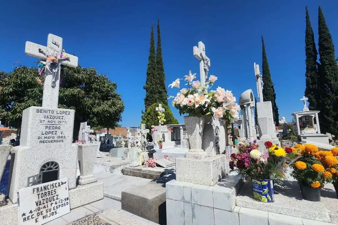 F ó tam graves y monumentos en cementerio con flores y símbolos religiosos en un día soleado.