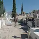 Tumba en cementerio con lápidas y cruces, rodeado de árboles cypress y en un día soleado.