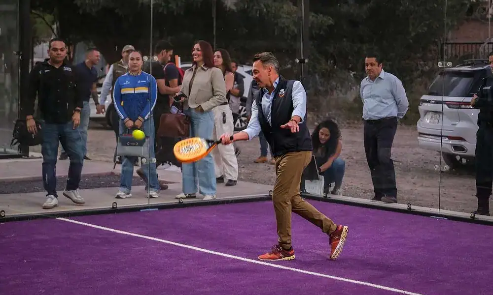 Deportista jugando pádel en cancha con espectadores observando.