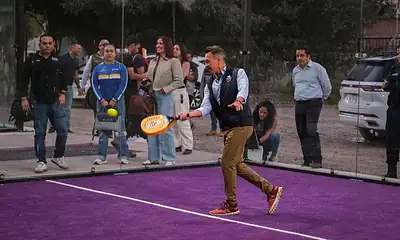 Deportista jugando pádel en cancha con espectadores observando.