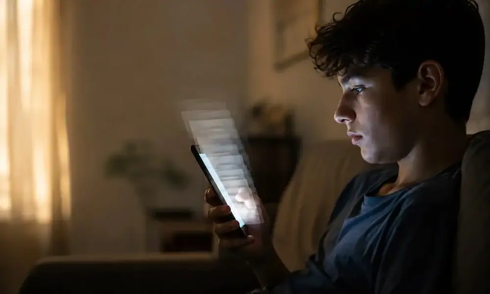 Un adolescente utiliza un teléfono celular mientras navega en redes sociales, en una imagen que ilustra el debate sobre el scroll infinito, advierte la SEP