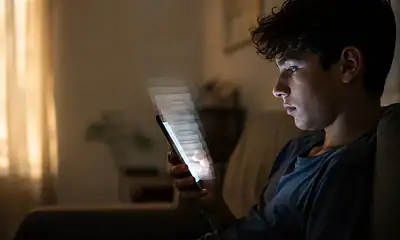 Un adolescente utiliza un teléfono celular mientras navega en redes sociales, en una imagen que ilustra el debate sobre el scroll infinito, advierte la SEP